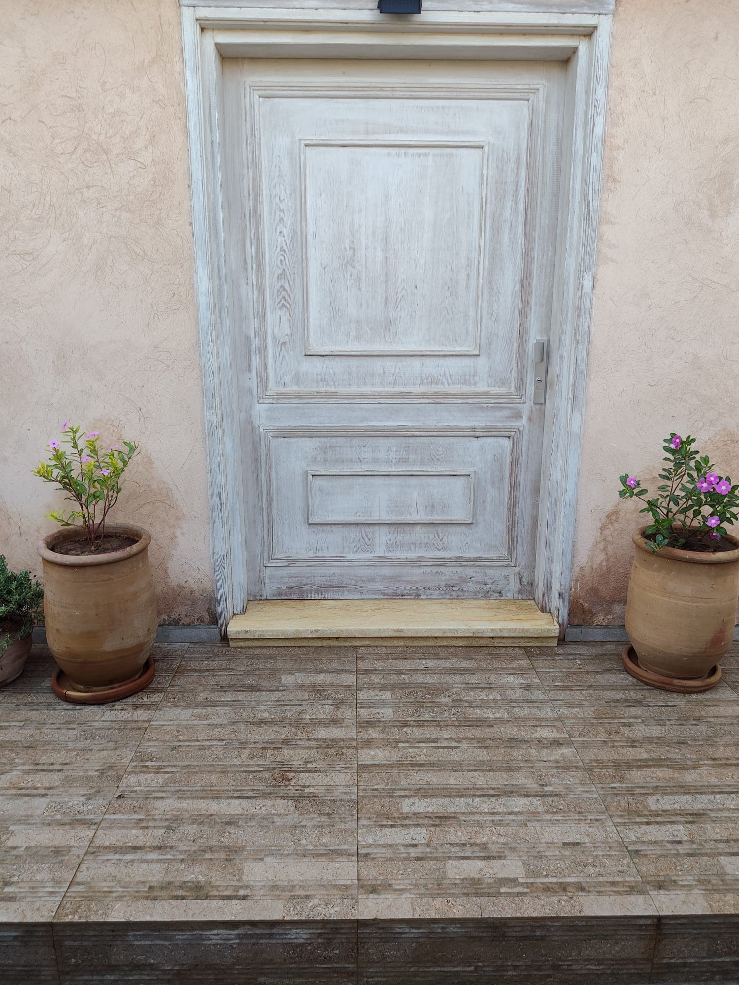 Pose de carrelage extérieur en grès cérame imitation pierre sur terrasse d'entrée, avec rénovation de porte en bois à effet vieilli et mise en place d'un seuil en pierre naturelle. Une entrée soignée alliant matériaux nobles et finitions artisanales qui dégage un charme méditerranéen authentique et raffiné.