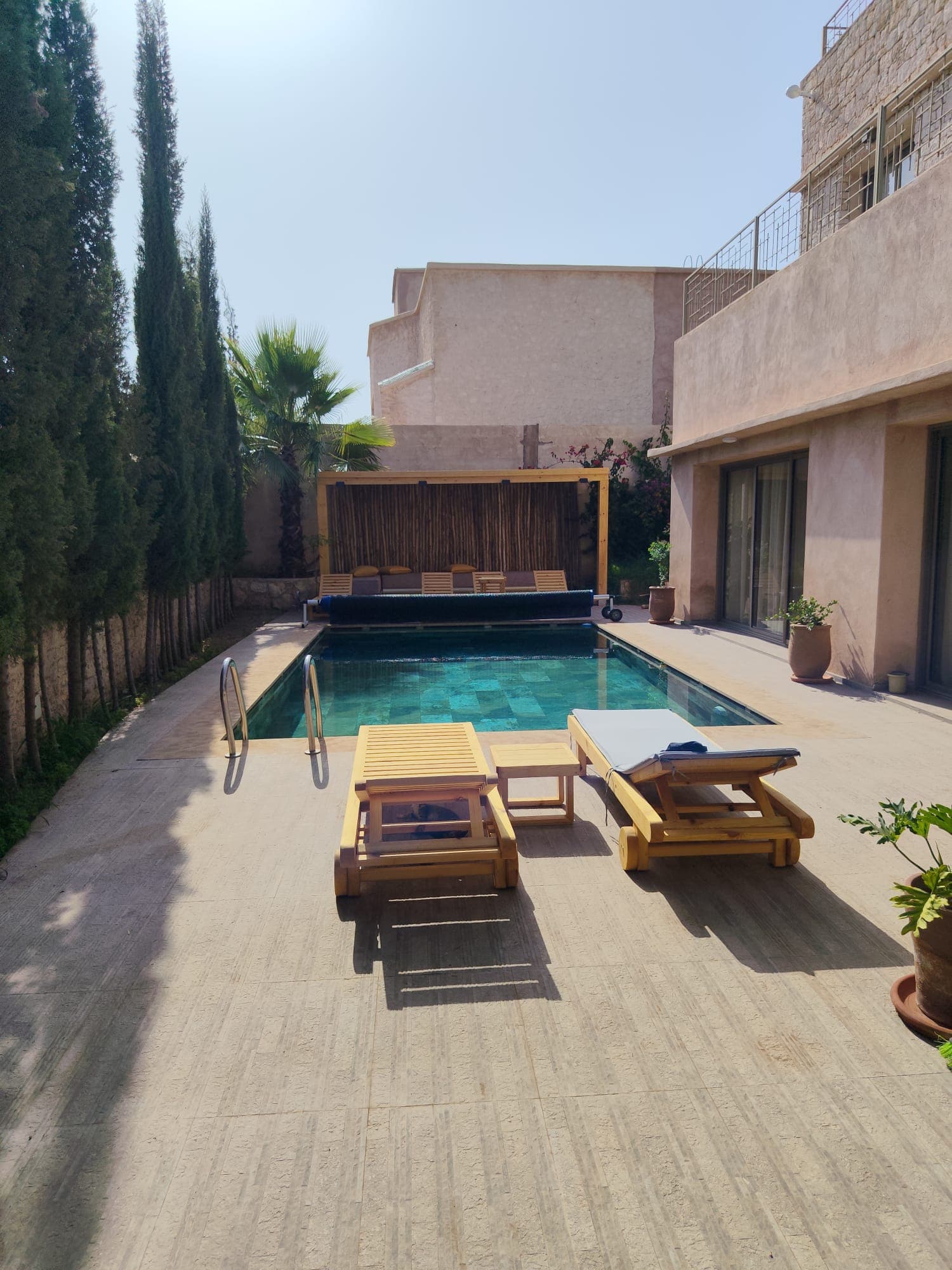 Réalisation d'une terrasse piscine avec dallage grand format en grès cérame imitation bois, équipée d'une pergola en bois et bambou avec brise-soleil intégré. Un espace extérieur haut de gamme alliant fonctionnalité et esthétique méditerranéenne, parfaitement mis en valeur par la qualité des finitions et l'harmonie des matériaux.